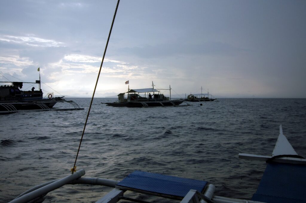 Tre banca da immersione all'ormeggio su Monad Shoal sotto un cielo grigio di primo mattino, viste dal ponte di un'altra barca