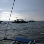 Tre banca da immersione all'ormeggio su Monad Shoal sotto un cielo grigio di primo mattino, viste dal ponte di un'altra barca