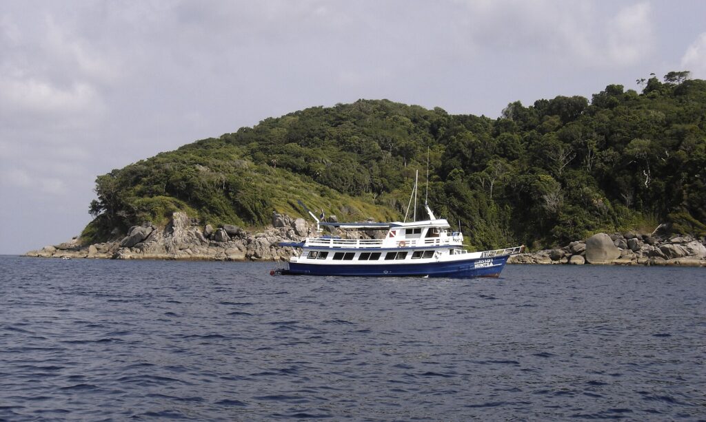 Una barca da crociera blu e bianca ancorata davanti a un'isola delle Similan, con i massi di granito grigi a pelo d'acqua sotto la foresta
