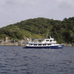 Una barca da crociera blu e bianca ancorata davanti a un'isola delle Similan, con i massi di granito grigi a pelo d'acqua sotto la foresta
