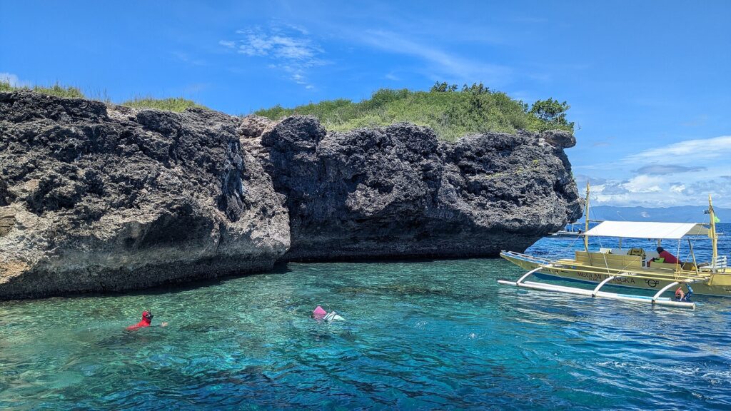 La falesia calcarea grigia e scavata dell'isola di Pescador, due persone che nuotano con maschera e boccaglio e una banca gialla in un'acqua turchese