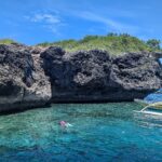 La falesia calcarea grigia e scavata dell'isola di Pescador, due persone che nuotano con maschera e boccaglio e una banca gialla in un'acqua turchese
