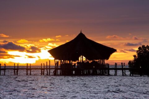 Il padiglione con il tetto di paglia del Fundu Lagoon, su palafitte in fondo al pontile, al tramonto