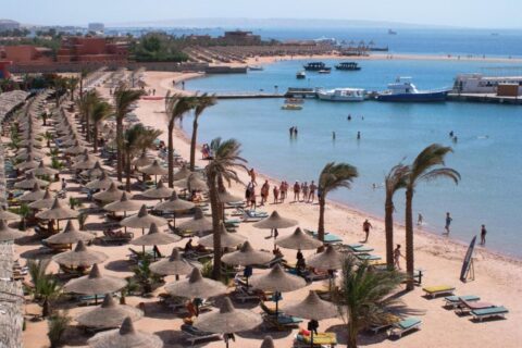 La spiaggia del Giftun Azur Resort, con gli ombrelloni di paglia e le palme, un pontile e alcune barche sullo sfondo