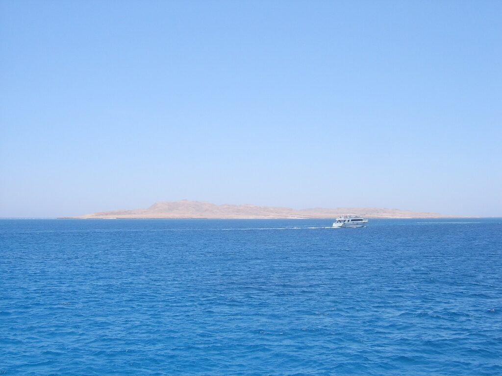 L'isola piatta e desertica di Giftun Soraya vista dal mare, con una barca da immersione bianca che le passa davanti