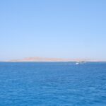 L'isola piatta e desertica di Giftun Soraya vista dal mare, con una barca da immersione bianca che le passa davanti