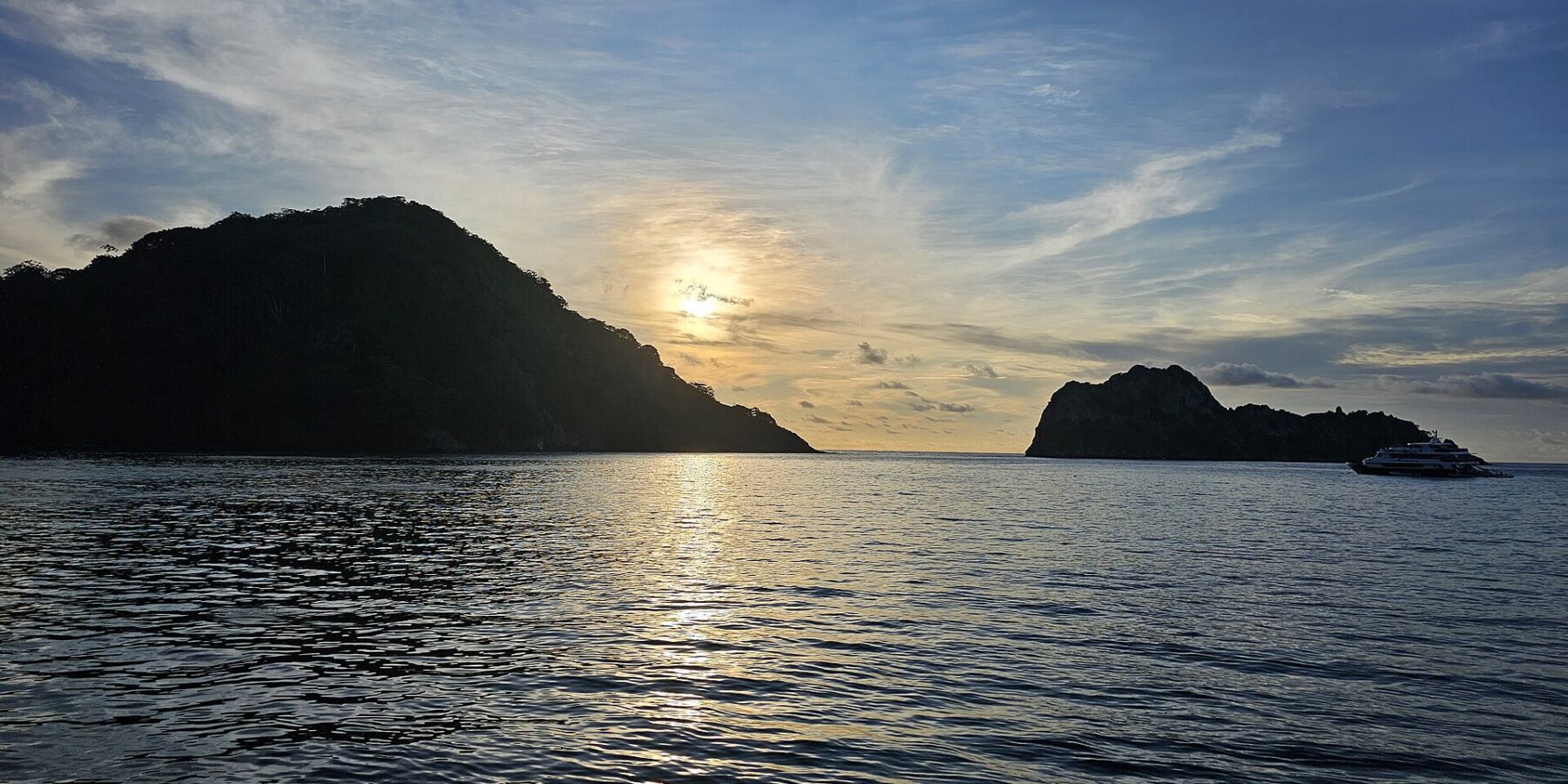 L'isola del Cocco in controluce al tramonto, con una barca da crociera all'ancora sulla destra e il mare calmo