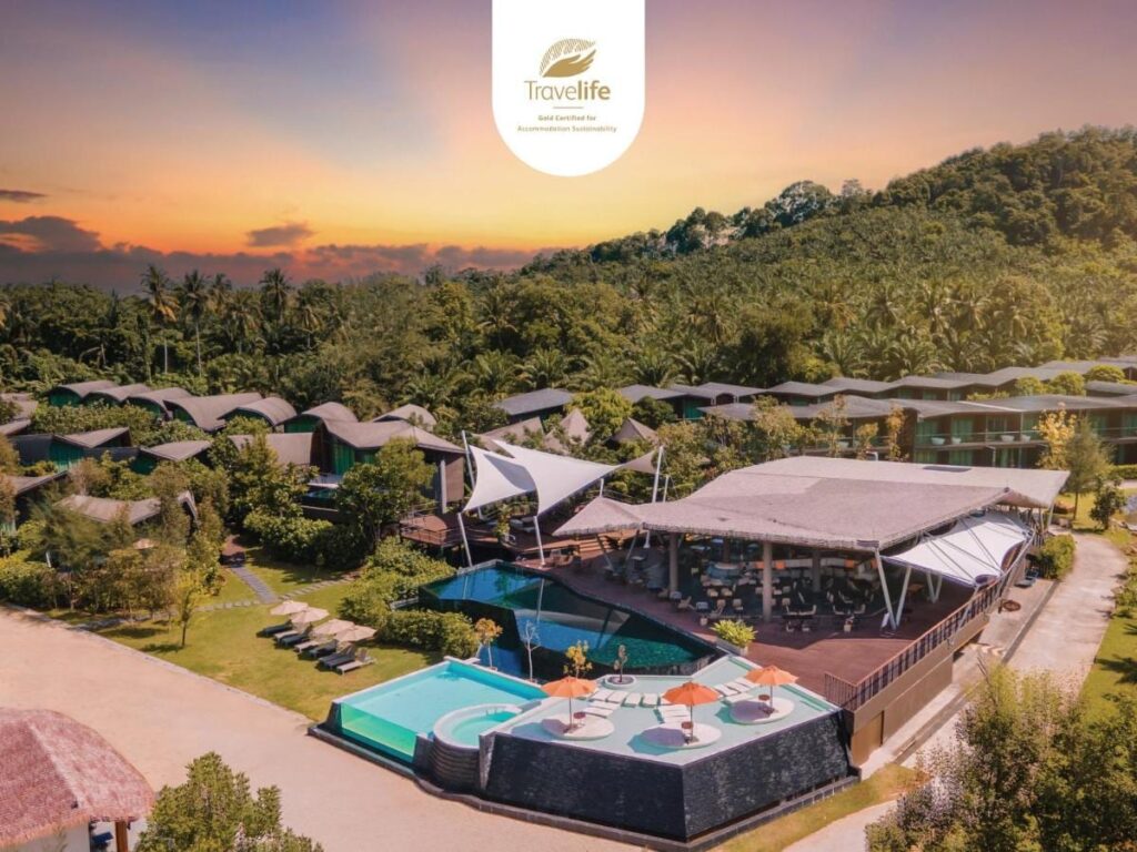 Vista aerea del Kalima Resort Khao Lak al tramonto, con le piscine e i tetti curvi ai piedi di una collina boscosa