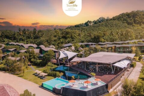 Vista aerea del Kalima Resort Khao Lak al tramonto, con le piscine e i tetti curvi ai piedi di una collina boscosa