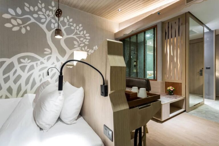 Un letto ai piedi di una parete dipinta con un albero bianco, con una lampada da lettura
