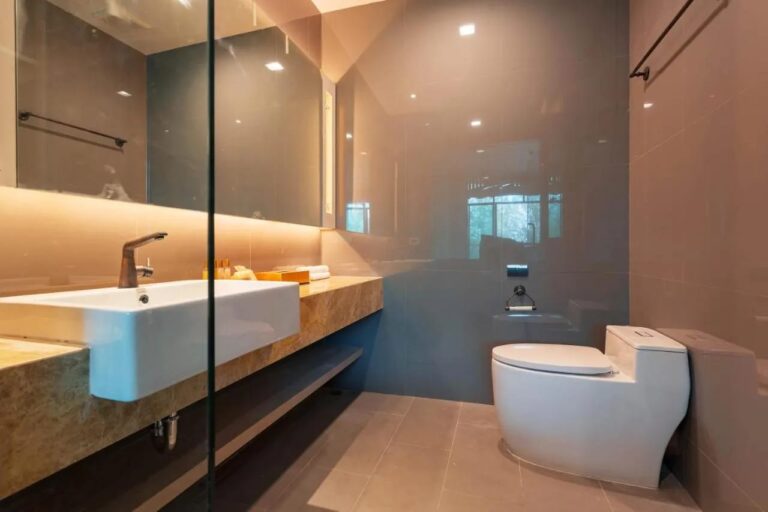 Un bagno con un lavabo su un piano in marmo, uno specchio illuminato e un WC