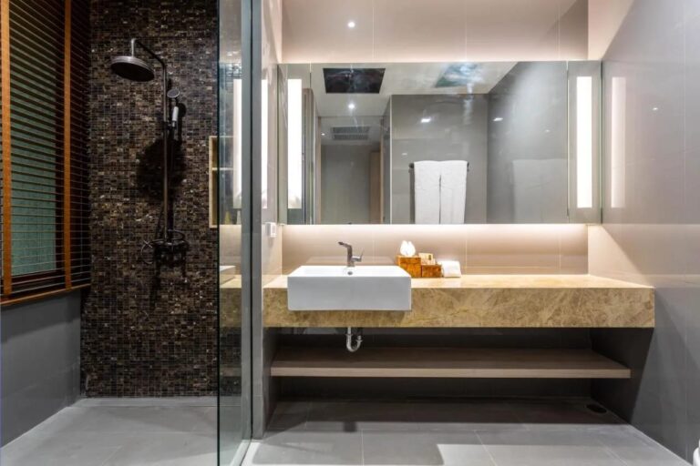 Una doccia contro una parete a mosaico scuro, accanto a un lavabo sotto uno specchio illuminato