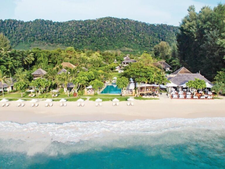 Il Layana Resort visto dal mare, con la spiaggia, gli ombrelloni bianchi, la piscina e i tetti sotto le palme