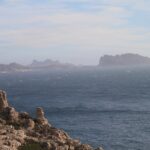 Dalle rocce calcaree del Frioul in primo piano, vista su un mare agitato e spumeggiante fino all'isola Maïre e alla costa di Les Goudes, nella foschia.