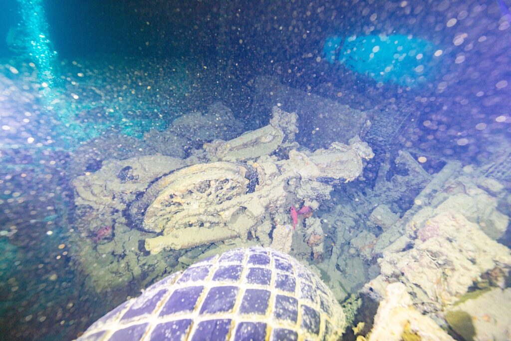 In una stiva buia del Thistlegorm, una moto rovesciata dietro uno pneumatico di camion, illuminata dalla torcia