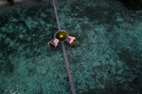 Vista aerea notturna di un lungo pontile in legno che parte dalla spiaggia, con due capanne su palafitte a metà strada