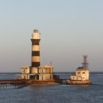 Il faro di Daedalus, una torre a strisce bianche e nere sul reef, con i suoi edifici e il pontile metallico, al tramonto