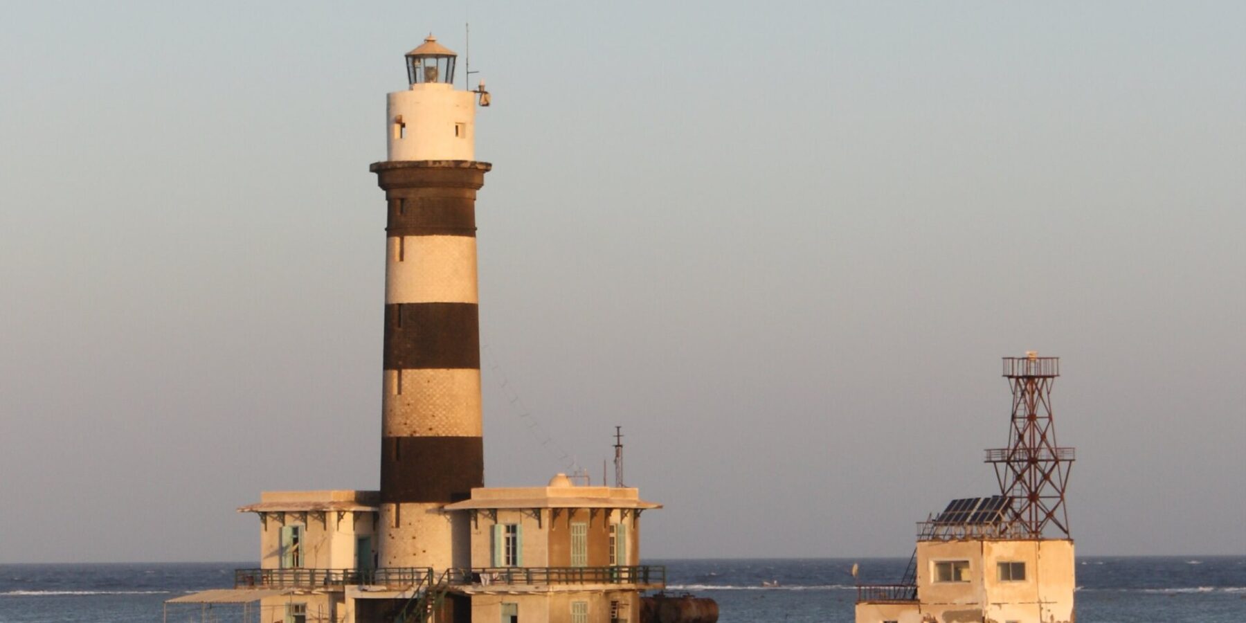 Il faro di Daedalus, una torre a strisce bianche e nere sul reef, con i suoi edifici e il pontile metallico, al tramonto