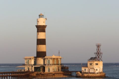 Il faro di Daedalus, una torre a strisce bianche e nere sul reef, con i suoi edifici e il pontile metallico, al tramonto