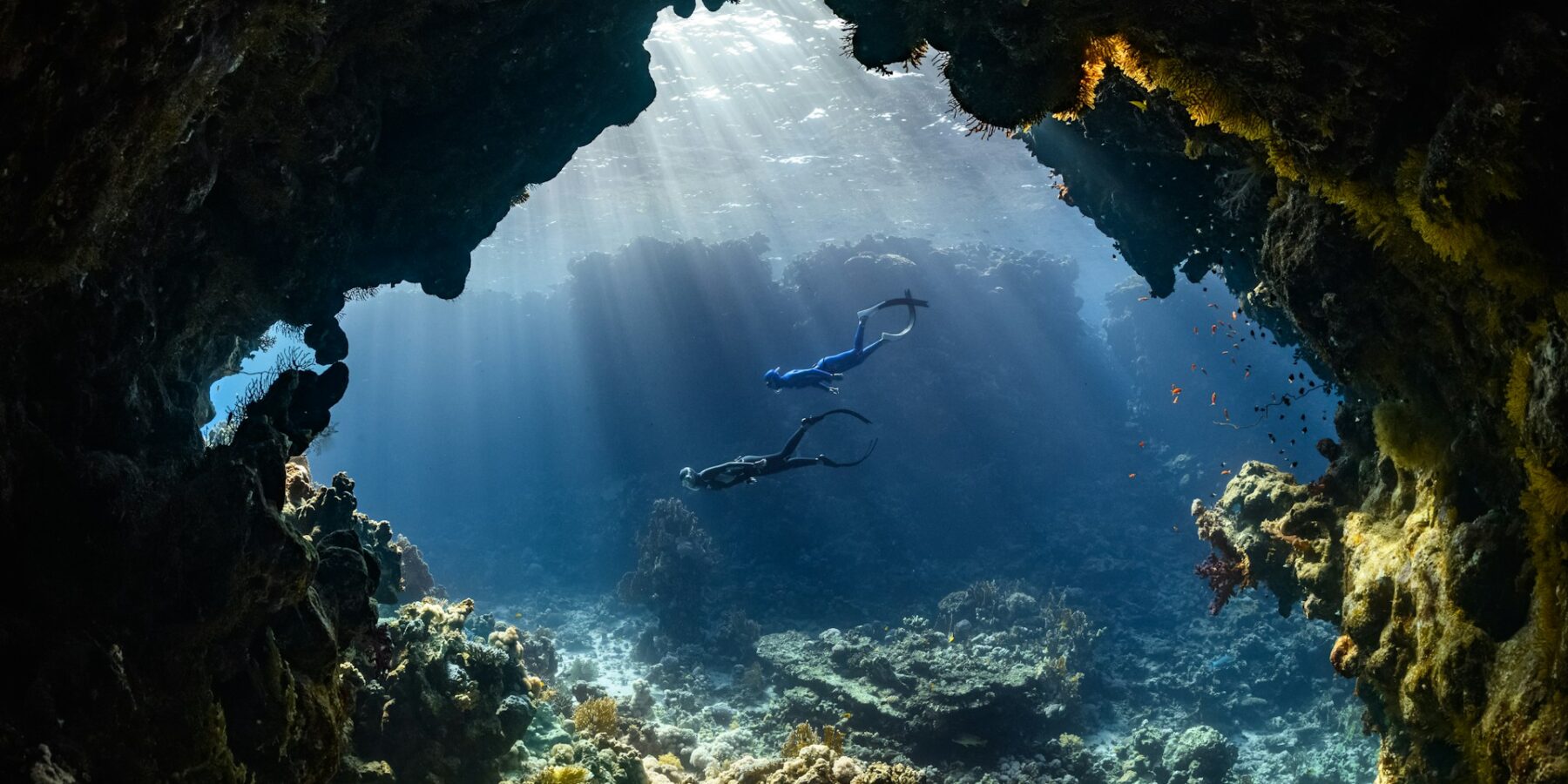 Due sub attraversano una grotta sottomarina illuminata dai raggi del sole, sopra una barriera corallina