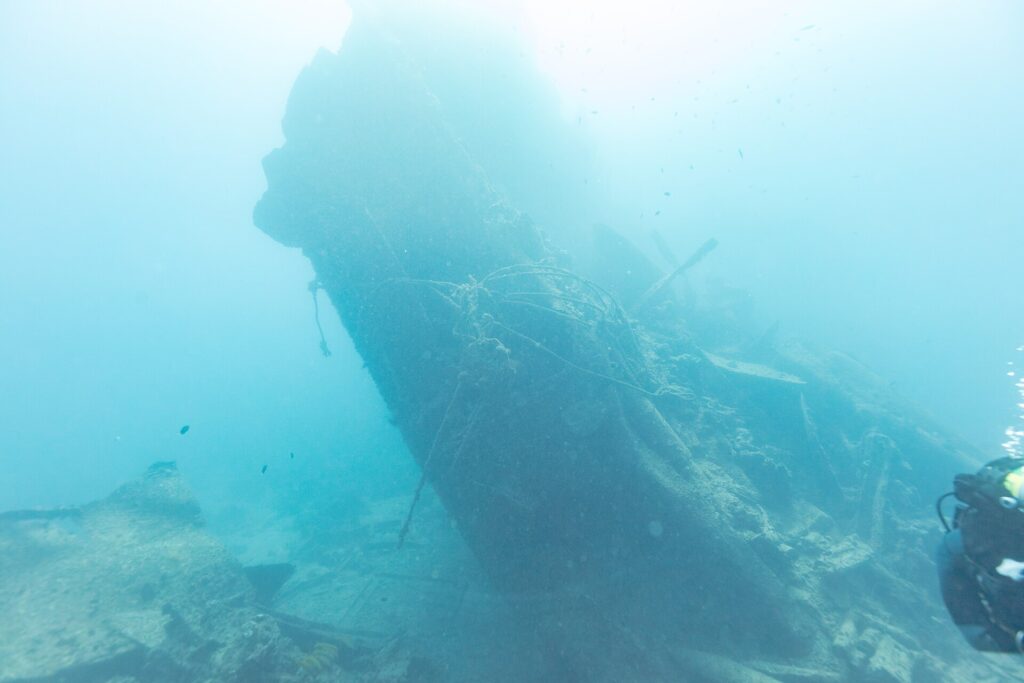 La poppa spezzata del Thistlegorm che si alza inclinata nel blu, con un sub sulla destra