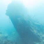 La poppa spezzata del Thistlegorm che si alza inclinata nel blu, con un sub sulla destra