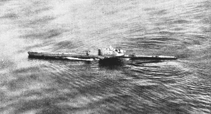 Foto d'archivio in bianco e nero, scattata da un aereo, di un sommergibile che fila in superficie su un mare increspato, con la scia lungo lo scafo e la torretta al centro.