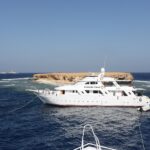 Tre barche da crociera ormeggiate davanti all'isolotto piatto di Small Brother, con il faro di Big Brother visibile all'orizzonte
