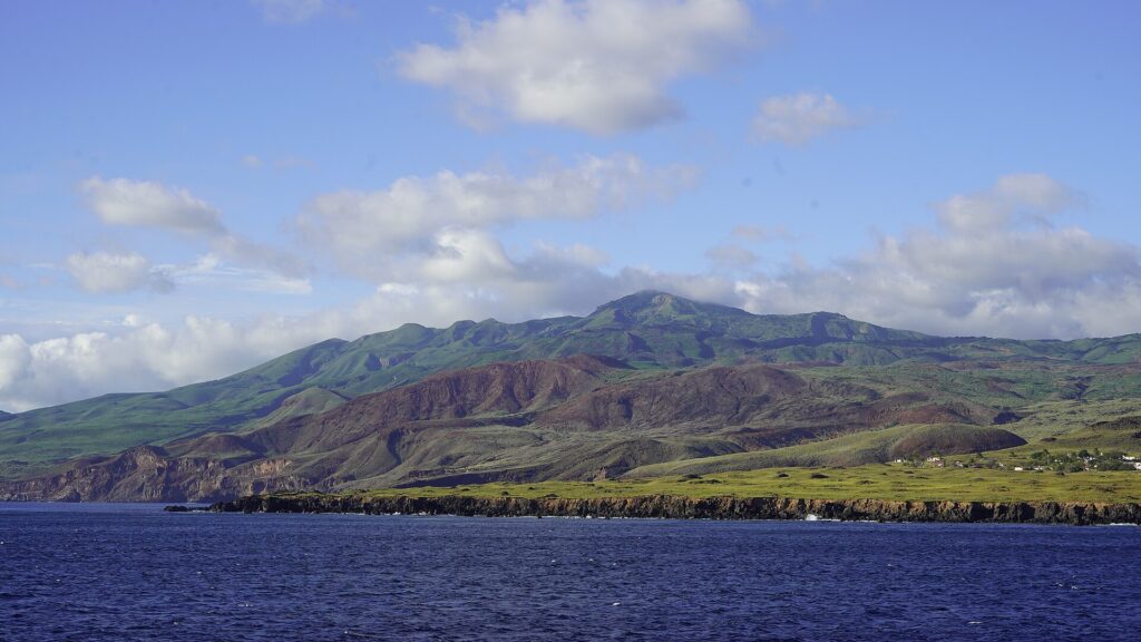 La costa dell'isola Socorro vista dal mare: falesie di lava nera, colline verdi e rossicce e la cima del vulcano tra le nuvole