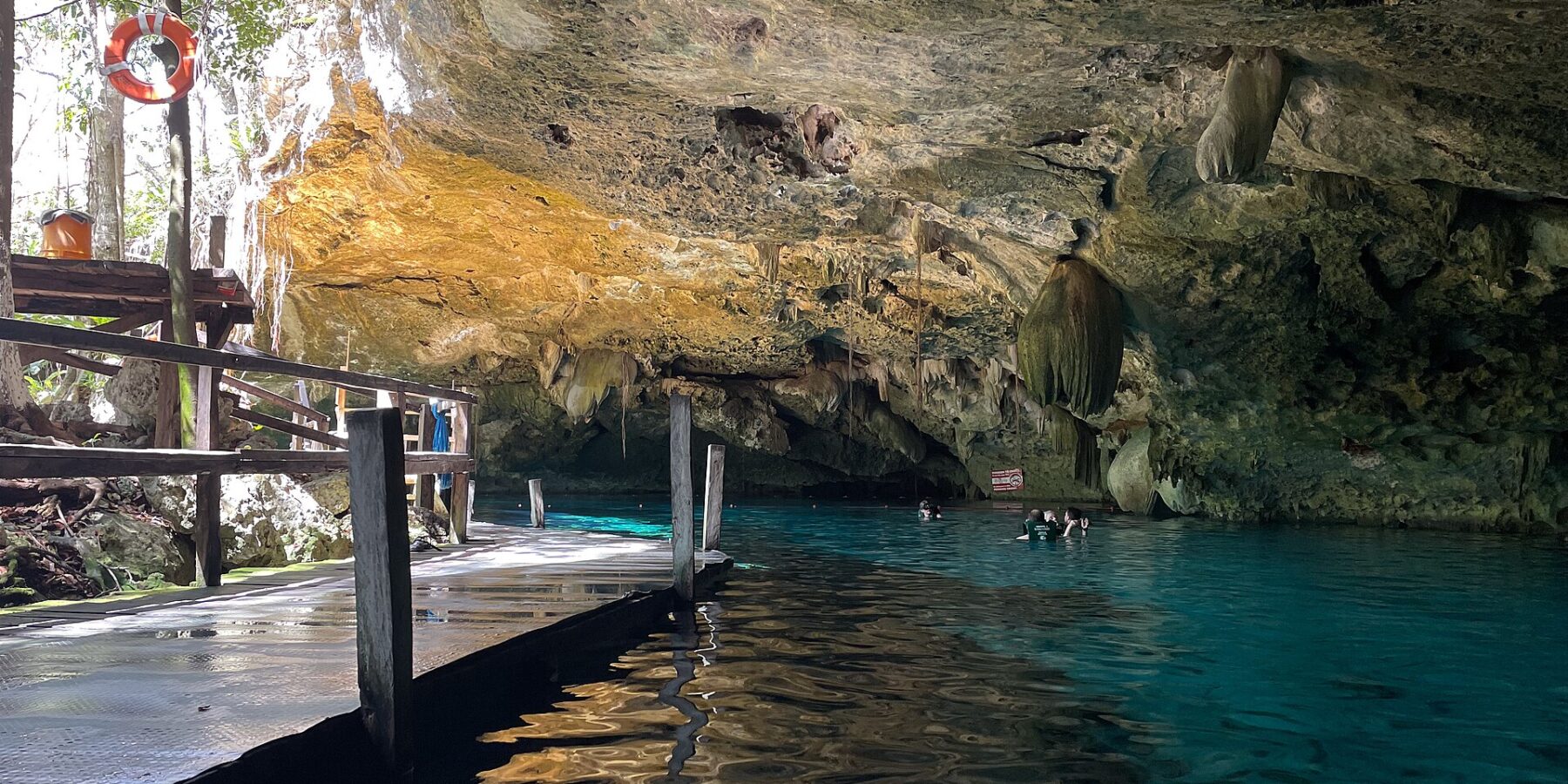 L'occhio est del cenote Dos Ojos: una volta di calcare irta di stalattiti sopra un'acqua turchese, un pontile di legno a sinistra e dei nuotatori sullo sfondo