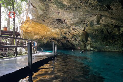 L'occhio est del cenote Dos Ojos: una volta di calcare irta di stalattiti sopra un'acqua turchese, un pontile di legno a sinistra e dei nuotatori sullo sfondo