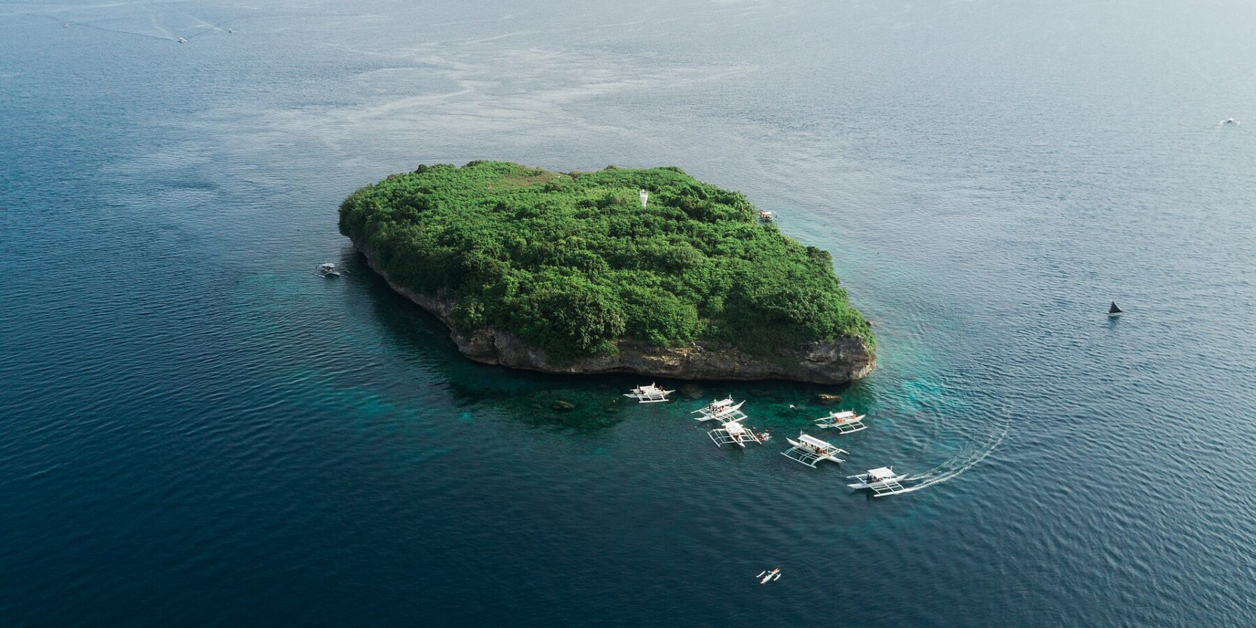 Vista aerea dell'isola di Pescador, uno scoglio coperto di vegetazione verde con il suo faro bianco, circondato da una decina di banca da immersione su un mare blu scuro