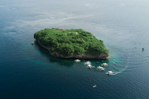 Vista aerea dell'isola di Pescador, uno scoglio coperto di vegetazione verde con il suo faro bianco, circondato da una decina di banca da immersione su un mare blu scuro