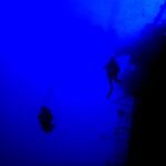 Nel blu profondo, due sub in controluce costeggiano il parapetto della poppa del Salem Express, con il ponte inclinato a destra