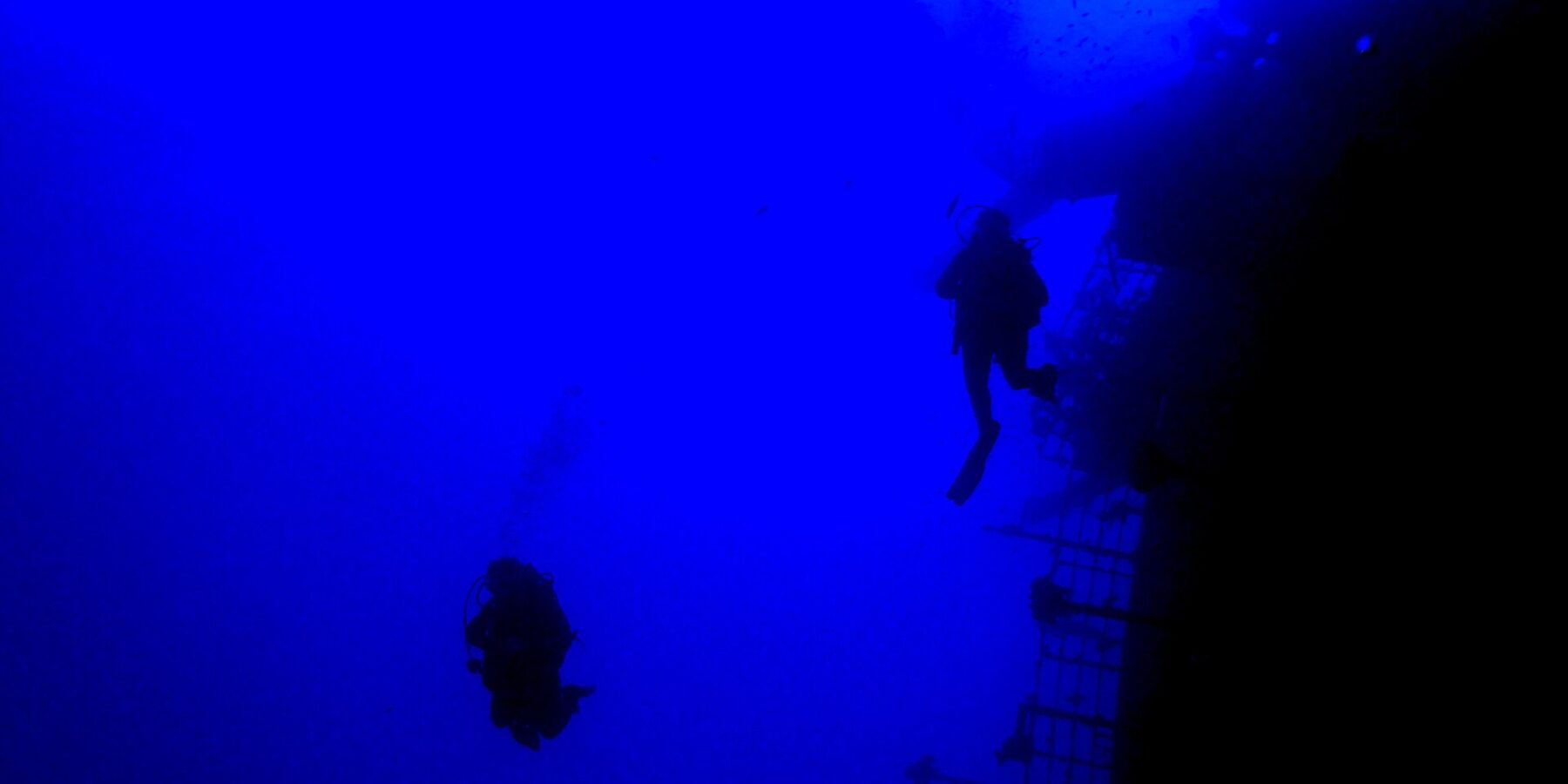 Nel blu profondo, due sub in controluce costeggiano il parapetto della poppa del Salem Express, con il ponte inclinato a destra