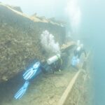 Due sub costeggiano il ponte del Thistlegorm lungo un corridoio, in un'acqua blu lattiginosa
