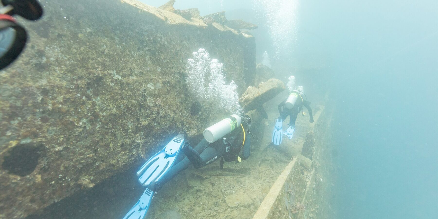 Due sub costeggiano il ponte del Thistlegorm lungo un corridoio, in un'acqua blu lattiginosa