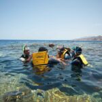 Nuotatori con giubbotti gialli, maschera e boccaglio nell'acqua limpida del Blue Hole, con le montagne del Sinai dietro